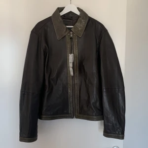 Svart skinnjacka från Zara - Säljer en svart skinnjacka från Zara i 100% läder. Jackan har klassisk krage, dragkedja framtill och diskreta detaljer i samma färg. Perfekt för dig som gillar stilren och tidlös design.