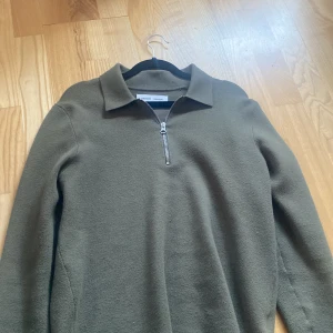 Olivgrön tröja med dragkedja från Samsøe Samsøe - Säljer en olivgrön långärmad tröja från Samsøe Samsøe med krage och dragkedja framtill. Tröjan har en klassisk passform och är tillverkad i ett mjukt material som passar perfekt till kalla vårkvällar 