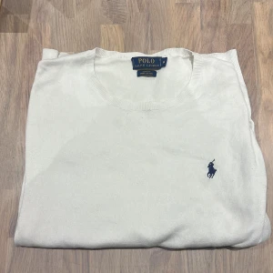 Vit tröja från Polo Ralph Lauren - Vit långärmad tröja från Polo Ralph Lauren i slim fit-modell. Tillverkad i mjuk pima bomull och har den klassiska blå broderade loggan på bröstet. Perfekt för en clean och stilren look till sommaren. Polo märket i nacken är påsytt pga att den lossnat.