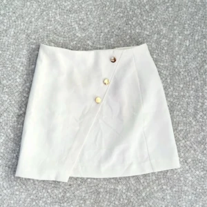 Vit kjol med knappar från Amisu - Snygg vit kortkjol från Amisu med tre dekorativa knappar framtill. Kjolen har en stilren look och passar perfekt till många olika outfits. 