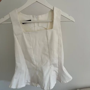 Korsett-topp - Snygg vit korsett-topp med fyrkantig ringning och dragkedja bak. Modellen är figurnära och har en lätt utsvängd nederkant