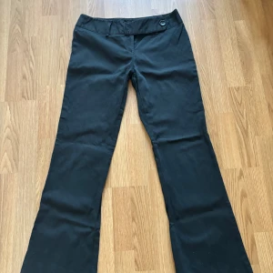 Svarta kostymbyxor från Lindex - Snygga svarta kostymbyxor från Lindex med diskreta vertikala ränder. Byxorna har normal passform, raka ben och stängs med knapp och dragkedja. Perfekta för en stilren look.