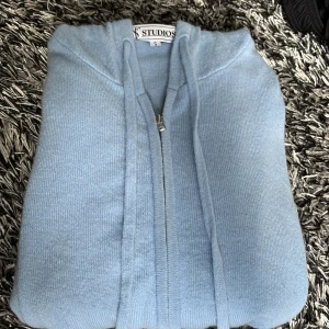 Ljusblå Kashmir hoodie med dragkedja från Studios - Mysig ljusblå hoodie från Studios i storlek S. Tröjan har dragkedja framtill, och är tillverkad i Kashmir. Perfekt för en avslappnad stil. storlek S och är i fint skick 
