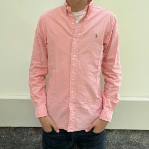 Polo Ralph Lauren skjorta - Säljer en ljusrosa skjorta från Polo Ralph Lauren i slim fit-modell. Skjortan har långa ärmar, klassisk krage och knappar framtill. Broderad logga på bröstet. Perfekt för en stilren look.