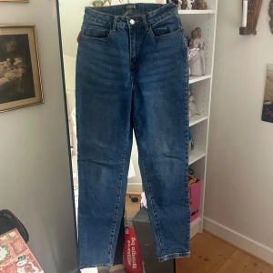 Blå raka jeans från Even & Odd - Klassiska blå jeans från Even & Odd med fem fickor och raka ben. Byxorna har hög midja och stängs med knapp och dragkedja. Perfekta för en avslappnad och stilren look. Använda en del men i mycket bra skick. 99% bomull och 1% elastan, därav lite stretch.