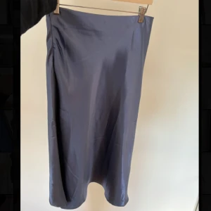 Mörkblå satinkjol - Säljer en stilren mörkblå satinkjol med midilängd och rak passform. Kjolen har en lätt glansig yta och faller snyggt längs kroppen. Perfekt att matcha med en enkel topp eller stickad tröja.