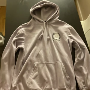 Ljuslila hoodie från H&M - Säljer en ljuslila hoodie från H&M i regular fit. Tröjan har huva med dragsko, magficka och ett litet tryck på bröstet. Perfekt för en avslappnad stil och enkel att matcha med jeans eller leggings.