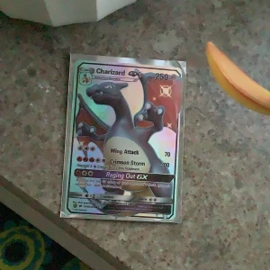 Charizard GX Pokémonkort - Säljer ett Charizard GX Pokémonkort med holografisk yta. Kortet har attacker som Wing Attack, Crimson Storm och Raging Out GX. Perfekt för samlare eller Pokémon-fans som vill utöka sin samling.