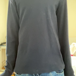 Mörkblå långärmad tröja - En enkel och stilren mörkblå långärmad tröja med rund halsringning. Tröjan har en diskret ribbad struktur och passar perfekt till jeans eller andra vardagsplagg. Perfekt basplagg i garderoben.