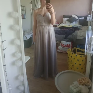 Ljusgrå axelbandslös / bandue långklänning/ balklänning  - Ljusgrå långklänning / balklänning med axelbandslös design. Finns ilägg i klänning så behövs ingen egen BH till. Fint skick då den inte används så ofta. Från Gina Tricot i storlek 34