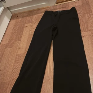 Svarta kostymbyxor från Vero Moda - Klassiska svarta kostymbyxor från Vero Moda med normal passform och raka ben. Byxorna har hällor för bälte och stängs med dragkedja och hake. Perfekta till en stilren look.