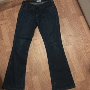 Mörkblå bootcut jeans från Lee - Säljer ett par mörkblå jeans från Lee med bootcut passform. Jeansen har klassiska fickor bak med Lee-logga och snygga kontrastsömmar. Perfekta för dig som gillar en tidlös och avslappnad stil.