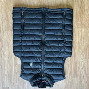 Svart dunväst - Snygg svart dunväst från U.S. Polo Assn med quiltad design och två dragkedjefickor framtill. Västen har broderad logga på bröstet och hel dragkedja. Perfekt för lager-på-lager under kyliga dagar.