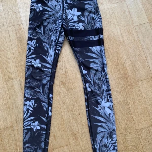 Svartvita blommiga träningstights från Stronger - Säljer ett par snygga träningstights från Stronger i svartvitt blommigt mönster som heter Pompeii. Materialet är en blandning av polyester och spandex.