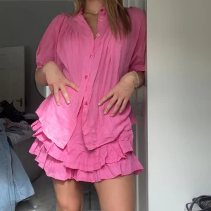 Rosa volangkjol och blus sett  - Supersöt rosa kjol + blus med volangdetaljer och dubbla lager. Kjolen är kort och har en luftig känsla, perfekt för varma dagar. Tillverkad i linne för en skön och sval känsla. 