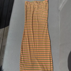 Randig långklänning vero Moda - Säljer en färgglad långklänning köpt på veromoda med smala ränder i grönt, orange, rosa och vitt. Klänningen är bandeau och har en tight passform med ribbad struktur. Storlek M