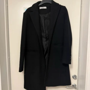 Svart kappa från Ellos - Säljer en klassisk svart kappa från Ellos med stilren design i storlek 36. Kappan har lång ärm, knappar vid ärmslut och två fickor framtill. Perfekt för dig som vill ha en tidlös och snygg jacka till garderoben.