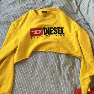 Gul croppad  sweatshirt från Diesel - Säljer en gul croppad långärmad tröja från Diesel med stort broderat logotyp-tryck på bröstet. Tröjan har rund halsringning och är perfekt för en trendig streetwear-look.
