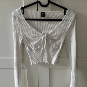 Vit ribbad croppad topp från SHEIN - Säljer en vit ribbad croppad topp från SHEIN med lång ärm och v-ringning. Toppen har knyt framtill som ger en snygg detalj och sitter tight. Perfekt till jeans eller kjol!
