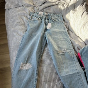 Ljusblå jeansbyxor med slitningar från 157 - Säljer ett par ljusblå jeansbyxor från 157 med snygga slitningar på benen. Byxorna har klassisk femficksdesign, raka ben och normal passform. Aldrig använda då de var lite för små :( passar mig super i längden, 175. Lite små i midjan. Är en L där :( 