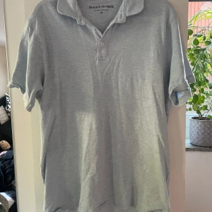 Ljusblå pikétröja från Bruun & Stengade - Säljer en ljusblå pikétröja från Bruun & Stengade i storlek XL. Tröjan har klassisk krage, knappar vid halsen och korta ärmar. Perfekt för en avslappnad och stilren look. Nypris 600kr