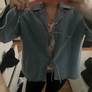 Ljusblå jeansjacka med knytning - Säljer en ljusblå jeansjacka med snygga råa kanter och knytning framtill istället för dragkedja eller knappar. Jackan har en avslappnad passform.