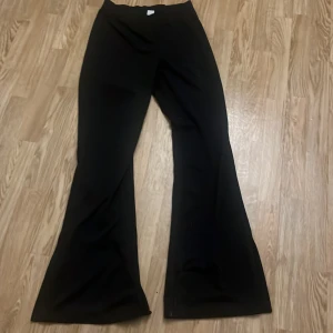 Svarta bootcut byxor i stretchigt material - Svarta bootcut byxor. Byxorna har hög midja och vida ben, samt en liten slit längst ner på benet. Lite av det tajtare hållet.