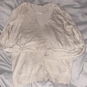 Beige v-ringad stickad tröja - Säljer en beige stickad tröja med v-ringning och långa ärmar. Tröjan har ribbade muddar vid ärmslut och nederkant, perfekt för lager-på-lager under kyligare dagar.