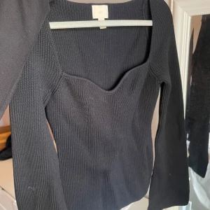 Svart ribbad topp från H&M - Säljer en svart ribbad topp från H&M med lång ärm och snygg sweetheart-urringning. Tröjan är figurnära och har en stretchig känsla, perfekt att styla till olika outfits.