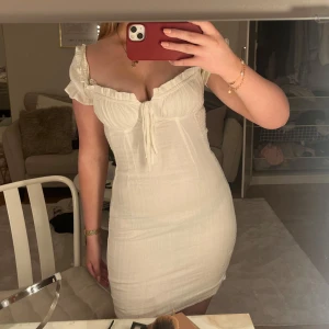 Vit offshoulder klänning - Supersöt vit kortklänning från Bikbok med offshoulder och volangdetaljer vid ärmarna. Klänningen har en tight passform och knyt framtill vid bysten. Mycker Stretchig och passar en XS-L men är i storlek S. Passar bra som tex studentklänning.