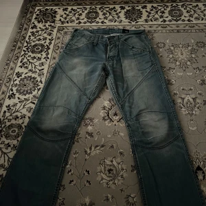 Jack and Jones jeans  - Snygga blåa Jack and Jones est 1975 jeans med unika sömmar och flera fickor. De har en cool design med extra sömmar över knäna och en knappdetalj på fickorna. Perfekta för en avslappnad stil. Finns ingen storlek på dem men om du bläddrar så ser man att midjan är 41,5cm. Säljs pågrund av att dem blivit för stora på mig. Priset kan diskuteras!