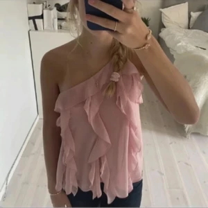Rosa oneshoulder topp med volanger - Säljer en söt rosa oneshoulder topp med volanger. Perfekt för en somrig look. Toppen har en luftig och lätt design som ger en romantisk känsla.
