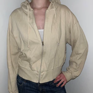 Beige hoodie från Lager 157 - Säljer en beige hoodie från Lager 157 med dragkedja och justerbar huva. Perfekt för en avslappnad stil. Den har långa ärmar och en bekväm passform.