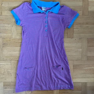 Randig klänning från WeSC - Säljer en kort randig klänning från WeSC i rosa och blått. Klänningen har korta ärmar och en klassisk krage med knappar framtill. Perfekt för en avslappnad stil. Finns hund och katt i hemmet.