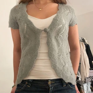 Grå stickad kofta - Säljer en söt grå stickad kofta med korta ärmar och en knapp framtill. Perfekt för lager-på-lager och ger en mysig känsla. Passar bra till både jeans och klänning.