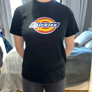 Svart t-shirt från Dickies - Säljer en klassisk svart t-shirt från Dickies med deras ikoniska logga i rött, gult och blått på bröstet. T-shirten har en normal passform och korta ärmar. Original pris är 300kr