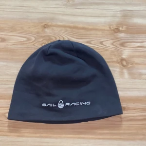 Svart mössa från Sail Racing - Snygg svart mössa från Sail Racing med broderad logga framtill. Perfekt för kyliga dagar med stilren design. Tillverkad i mjukt material för bekväm passform.