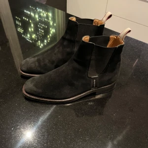 Svarta mocka Chelsea boots från Gant - Snygga svarta Chelsea boots i mocka från Gant. De har en klassisk design med elastiska paneler på sidorna och en dragflik baktill för enkel påtagning. Perfekta för en stilren look.