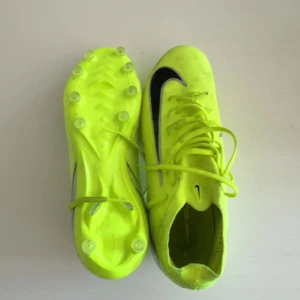 Nike Mercurial Air zoom 16 Pro AG Mad Energy Storlek 44 - Säljer ett par neon-gula fotbollsskor från Nike med svarta detaljer och snörning. Perfekta för att sticka ut på planen med sin iögonfallande färg och design.  Dessa är knappt använda och har inget som är sönder utan är bara smutsiga. (Priset kan förhandlas)