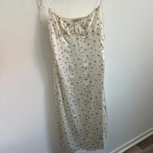Blommig sidenklänning  - Säljer en sidenklänning från nakd med ett fint blommönster i blått. Klänningen har en slits och smala axelband. Från Sanna Jörnviks kollektion 