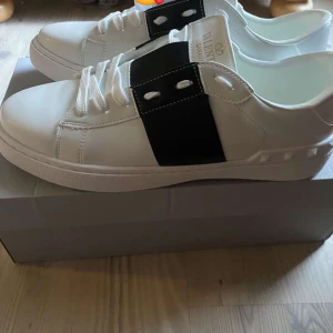 Valentino Garavani sneakers i vitt och svart - Snygga Valentino Garavani sneakers i vitt med en bred svart rem över snörningen. Skorna har en stilren design med vita snören och en bekväm sula. Perfekta för en trendig look köpte fel storlek tyvärr så helt nya passa på o köpa kom dm för mer information 🤩🤩