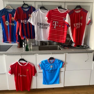 Samling av fotbollströjor från olika klubbar - Säljer en samling av fotbollströjor från olika klubbar. Tröjorna inkluderar bland annat blå och röda randiga, helröda och vita med olika klubbmärken. Perfekt för fotbollsfans som vill utöka sin garderob med klubbtröjor. De flesta tröjorna är kortärmade och finns i olika storlekar.