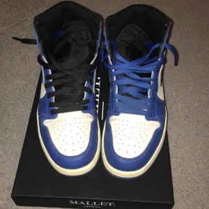 Nike Air Jordans i blått och vitt - Säljer ett par Nike Air Jordans i blått och vitt med svart swoosh. Skorna har hög modell med snörning och perforerad tå för ventilation. Perfekta för dig som älskar klassiska sneakers med en sportig look. Kan tvätta dom