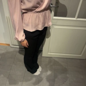 Rosa omlottblus - Säljer en elegant rosa omlottblus med långa ärmar och elastisk midja. Blusen har en v-ringad design och är perfekt för en stilren look.