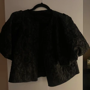 Svart blus med struktur och puffärm - Snygg svart blus med unik struktur och kortare ärmar. Använd endast en gång så i jättebra skick