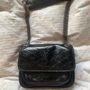 Svart axelväska från Saint Laurent - Snygg svart axelväska från Ysel Saint Laurent i skinn med kedjeaxelrem och ikonisk logga på framsidan. Väskan har ett stilrent och elegant utseende, perfekt för att lyfta din outfit. Den har ett huvudfack med plats för dina viktigaste saker. Har använt 2 gånger så den är som ny❤️