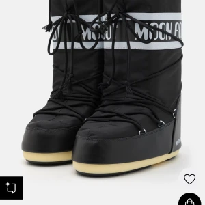Svarta Moon Boots - Säljer ett par svarta Moon Boots med snörning och vit logga. Perfekta för vintern med sin robusta design och bekväma passform. De har en unik stil som sticker ut och håller fötterna varma.
