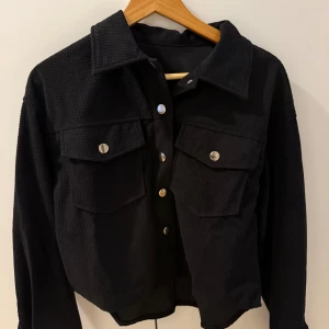 Svart tröja med knappar - Snygg svart jacka med knappar framtill och två bröstfickor. Jackan har en klassisk krage och är långärmad. Perfekt för en stilren look. Helt oanvänd och i storlek XS. Men modellen är lite oversize så mer som storlek S.