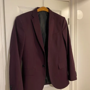 Vinröd kavaj från H&M - Snygg vinröd kavaj från H&M med klassisk design. Kavajen har en enkelknäppning och två framfickor. Perfekt för både formella och semi-formella tillfällen.