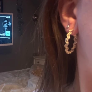 Guldiga örhängen med vågig design - Snygga guldiga örhängen i en vågig design. Perfekta för att ge en extra touch till din outfit. De är runda och har en unik struktur som fångar ljuset fint.